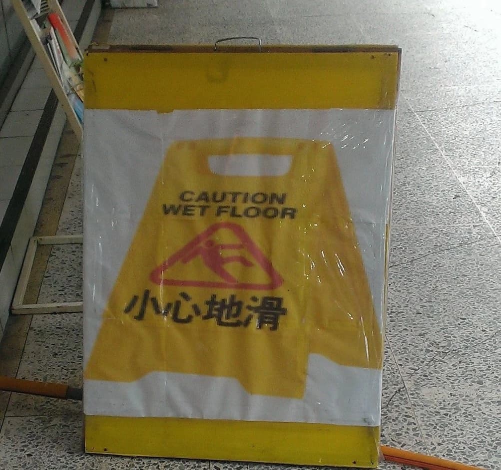 Photograph of a wet-floor sign printed on a protective cover over another sign